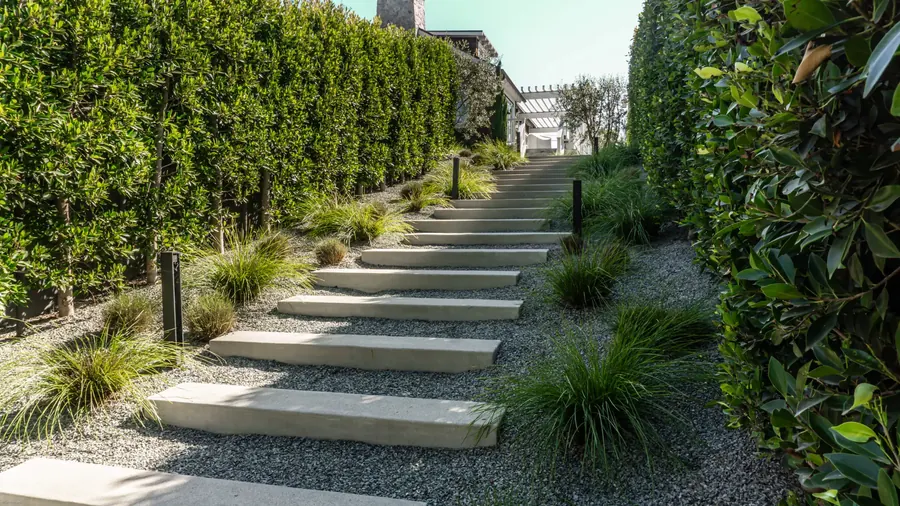 Concrete slab steps between clipped hedges and gravel on a hillside garden path