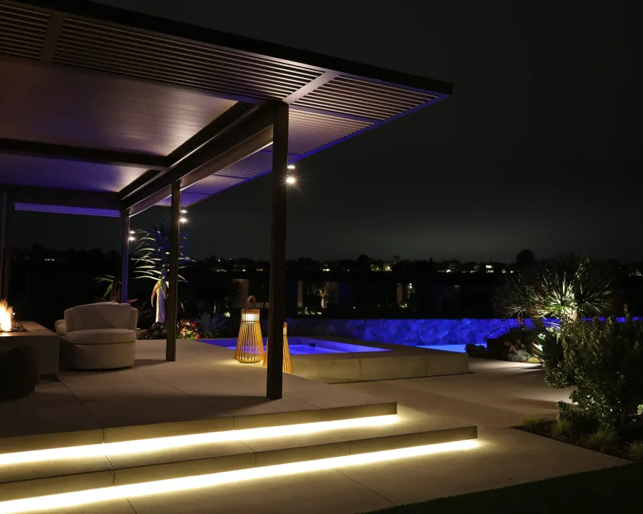 Illuminated step lights and a lit pergola beside a glowing blue pool at night